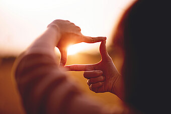 Eine Person bildet mit ihren Fingern einen Rahmen, den sie vor den Sonnenuntergang hält. Dies demonstriert den Blick in die Zukunft, die mit nachhaltigen Geschäftsmodellen gesichert ist