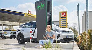 Tankstelle mit Ladestation, Frau sitzt vor Schnellladestation
